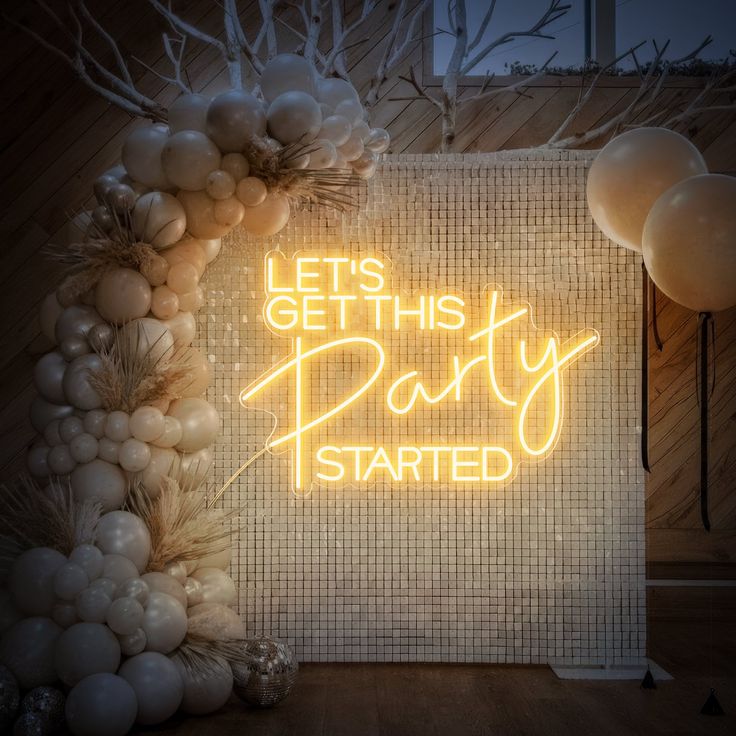 A let's get this party started neon sign in warm white hung up on a disco backdrop.