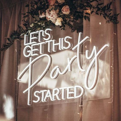 A neon sign hung up on a wedding backdrop with the words 'Let's get this party started' glowing  a cool white led glow